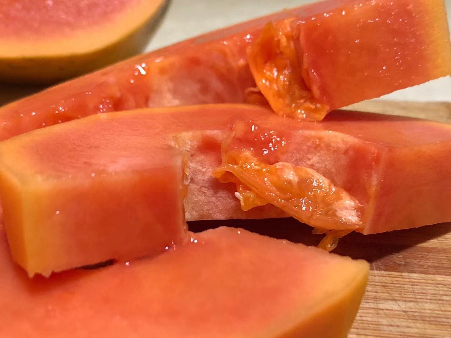 新鲜成熟红肉番木瓜(Carica papaya)横切实物图,展示典型可食部结构与天然色泽,用于直观理解‘每100克可食部’定义 红肉番木瓜横切特写:果肉呈均匀粉红色,质地细腻多汁,黑色圆形种子整齐排列于中央腔室,果皮浅绿色带蜡质光泽,背景为木质砧板与不锈钢水果刀