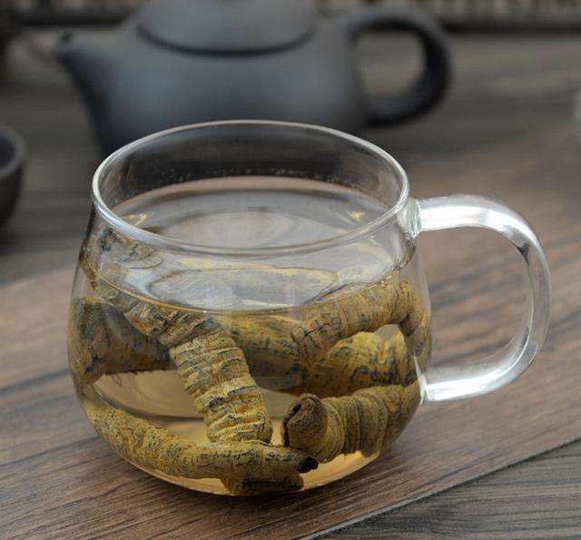 场景化摄影:透明耐热玻璃杯中,3克德庆巴戟天(棕褐色弯曲小段)与6克温县熟地黄(乌黑椭圆片)浸于浅琥珀色茶汤中;杯旁置食品级温度计显示水温90℃;杯盖严实,蒸汽轻微凝结于杯盖内壁 巴戟天熟地黄90℃焖泡过程示意图