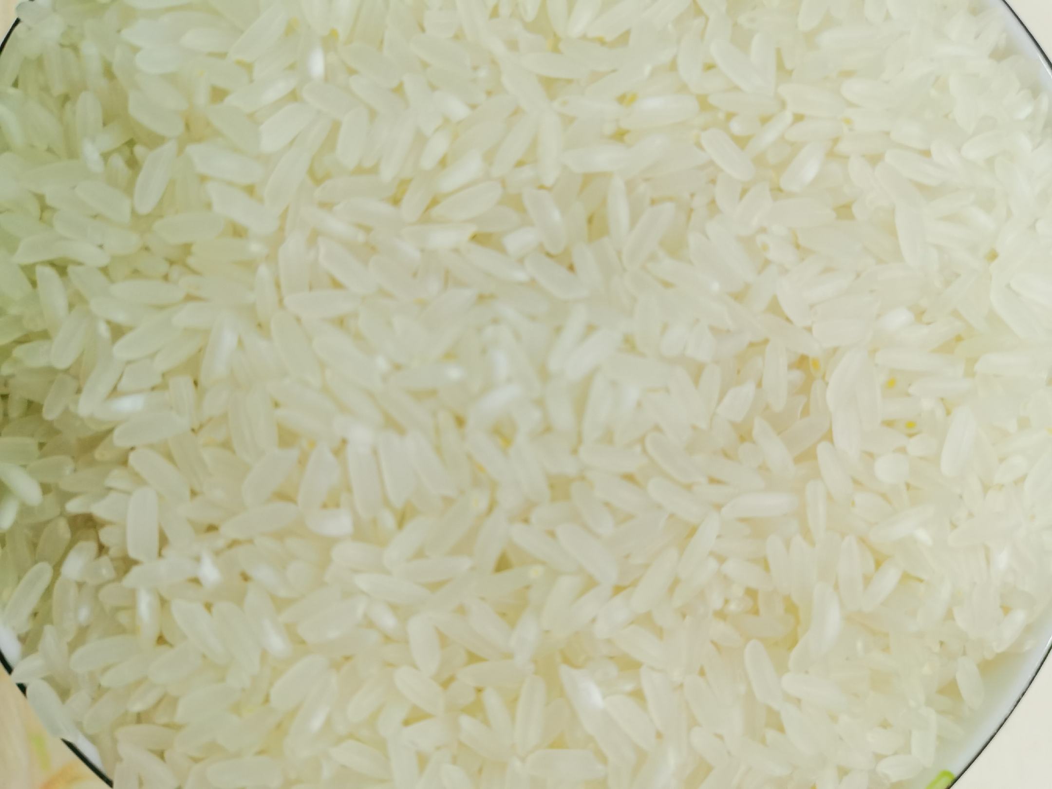 一碗刚出锅的长粒香米饭,热气腾腾,米粒分明且略带油光,旁边配有一双木筷和一小碟咸菜,营造温馨的家庭用餐氛围,突出米饭的诱人香气与质感 家庭厨房中煮好的长粒香米饭