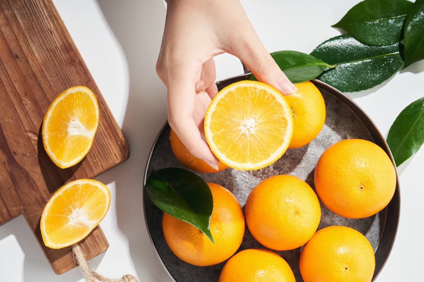 一个新鲜的冰糖橙被横向切开顶部,露出内部果肉,旁边有一把小勺正在小心地将橙肉挖出,保留完整的橙皮外壳,桌面整洁,光线柔和自然 橙子顶部切开并挖出果肉的过程