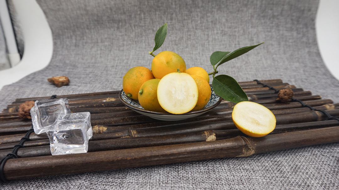 一幅生活美学风格的照片,展示金桔的不同用途:一部分用于泡水,杯中漂浮着切片金桔;一部分堆放在竹篮里;还有几颗正在被手工制作成果酱,旁边配有蜂蜜罐和玻璃瓶,营造温馨厨房氛围 金桔用途展示图