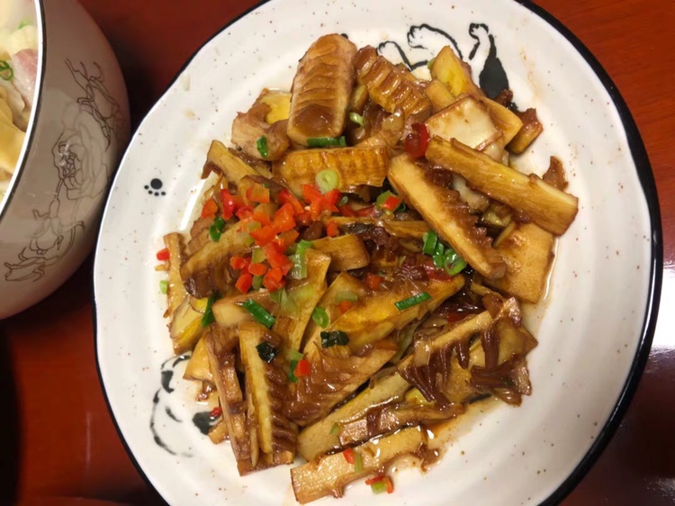 一位穿着围裙的农妇正在传统土灶前翻炒锅中的雷笋子,锅中热气腾腾,笋片与青红椒交错,旁边摆放着刚剥好的新鲜雷笋子和调味料,背景为木质橱柜与陶制碗碟,充满乡土生活气息 农家厨房中正在烹饪雷笋子的场景