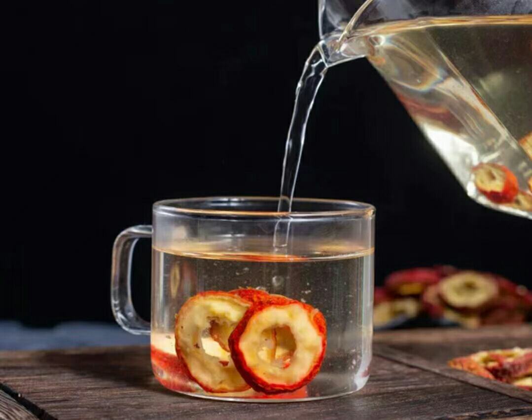 桌面上摆放着山楂干片、研磨成粉末的鸡内金、陶瓷煎药锅、玻璃杯中的褐色药茶,旁边配有量勺和标签纸,展示家庭自制山楂鸡内金茶的全过程 山楂鸡内金茶饮制作过程