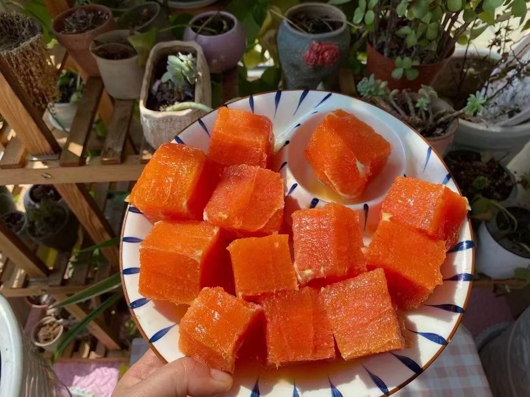 一张白色餐盘中摆放着多种血橙美食:左侧是整齐排列的血橙切片,中间是一杯深红色的血橙果汁,右侧是用血橙果肉制成的小罐果酱,旁边点缀着薄荷叶,背景虚化的厨房环境显得温馨整洁 血橙美食拼盘