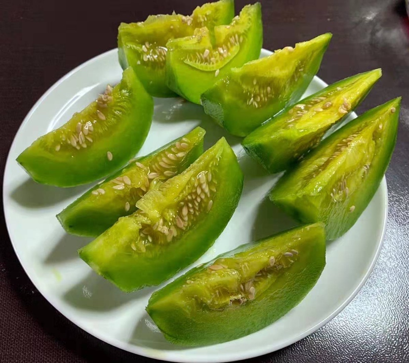 一盘精心摆盘的翠梨甜瓜切片,呈半月形排列,果肉洁白透明,表面泛着水润光泽,盘边点缀几片薄荷叶和蓝莓,背景为白色陶瓷餐盘与浅色厨房台面,整体风格清新自然,突出水果的新鲜与高级感 翠梨甜瓜切片摆盘