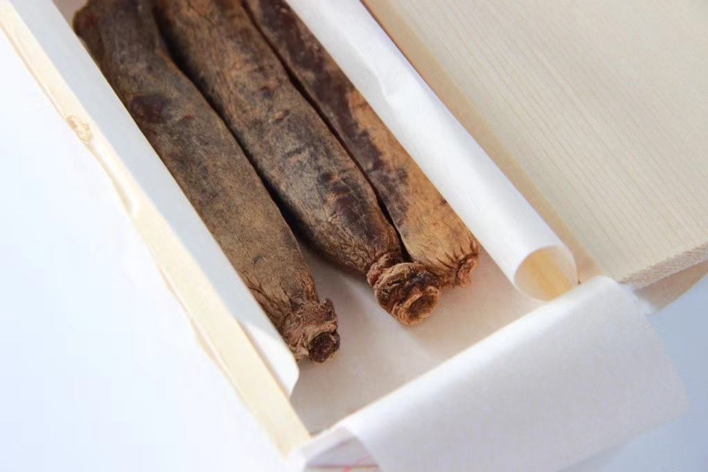 一瓶透明玻璃瓶装的深褐色红参浓缩液,标签标注‘红参元’字样,旁边摆放两粒红棕色胶囊和一片即食红参含片,背景为浅木色桌面,突显高端滋补品氛围 红参元产品展示图