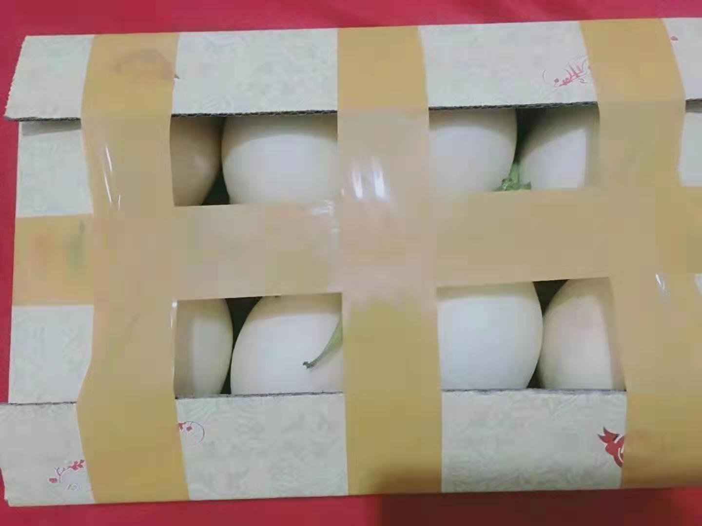 一张木质桌面上摆放着两款产品:左侧是印有‘东方蜜一号’字样的红色精美礼盒,右侧是透明餐盒装的黄色蜜瓜切块,旁边配有小勺和绿叶装饰,背景虚化的超市货架上陈列同类商品 东方蜜一号香瓜礼盒与切果展示