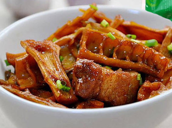 图片说明:一道家常笋干烧肉菜肴特写,深褐色酱汁包裹着软糯的笋干和肥瘦相间的五花肉块,旁边点缀绿色蒜苗,使用白色瓷碗盛装,置于原木纹理桌面上,背景虚化,突出食物色泽与质感 一碗炖好的笋干烧肉,深棕色汤汁浓郁,笋干吸饱油脂,配以青蒜点缀,摆放在木质餐桌上