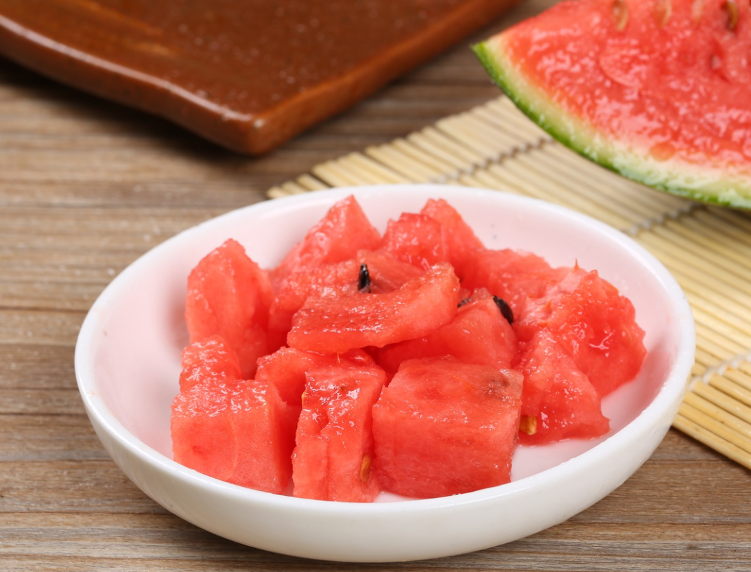 一颗切开的早春红玉迷你西瓜,露出鲜艳的红色瓜瓤,汁水饱满,果肉细腻,周围摆放着绿叶装饰,背景为浅色木质餐桌,整体画面清新自然,突出水果的新鲜与甜美 早春红玉迷你西瓜特写