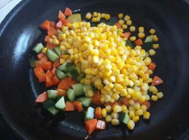 一位厨师正在不粘锅中翻炒混合食材,包括黄色速冻甜玉米粒、红色甜椒丁、绿色豌豆和鸡蛋碎,锅边摆放着未开封的速冻甜玉米包装袋,突出便捷健康的家常做法 家庭厨房中用速冻甜玉米制作五彩蔬菜炒饭场景