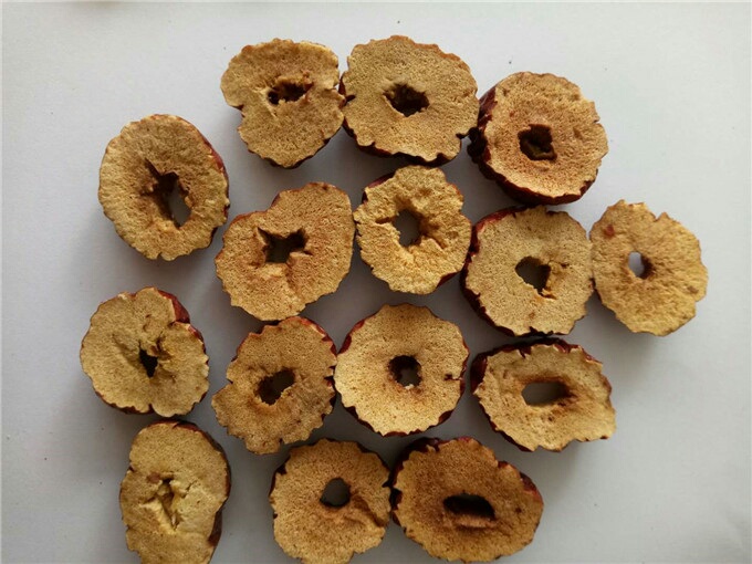 一个干燥完整的干红枣片被横向切开,露出内部呈浅褐色至深褐色的果肉,果核清晰可见,表面无霉斑或潮湿痕迹,背景为木质砧板,光线柔和自然 干红枣片横切面特写