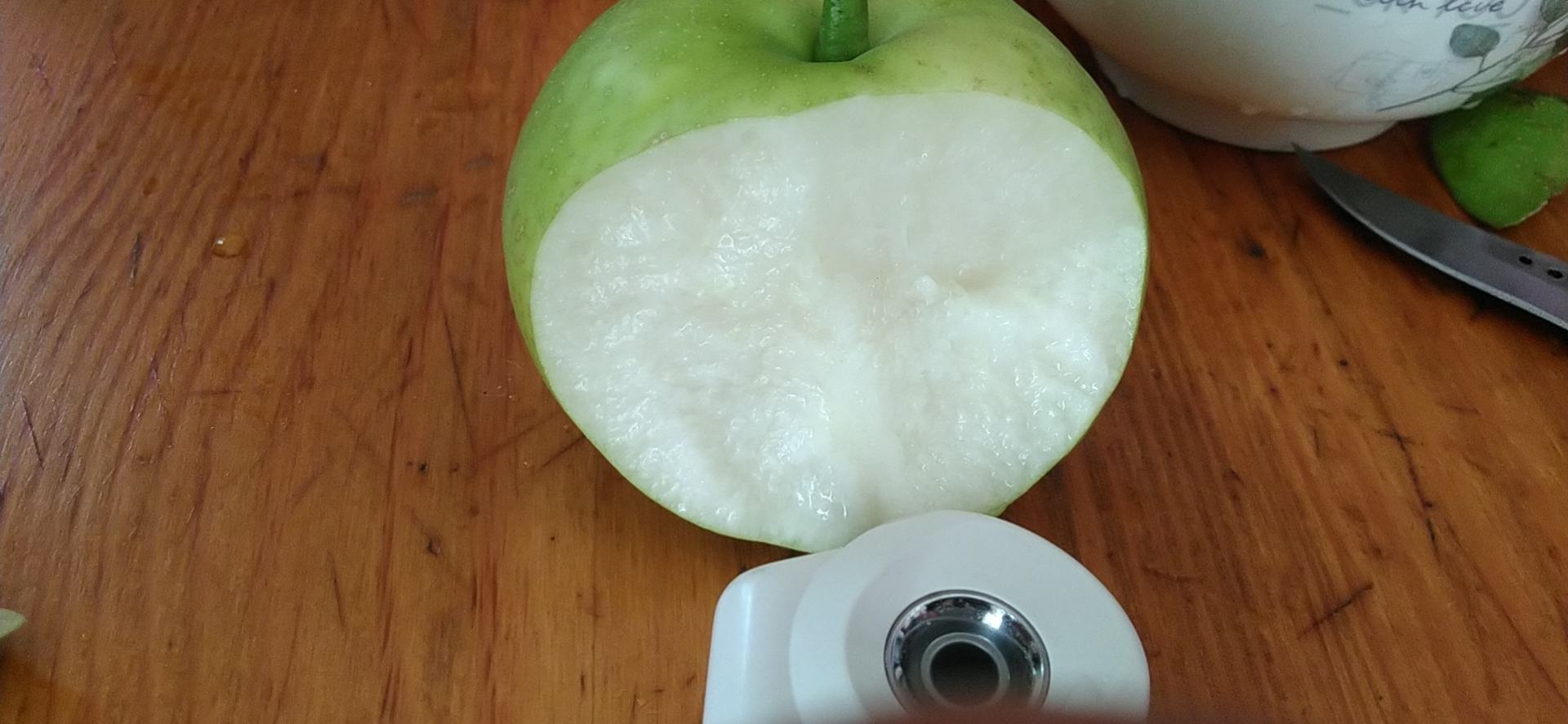 一颗被横向切开的酸梨,露出乳白色果肉和中心木质化果核,刀口处可见少量汁液渗出,背景为木质砧板和自然光线 酸梨切面细节展示