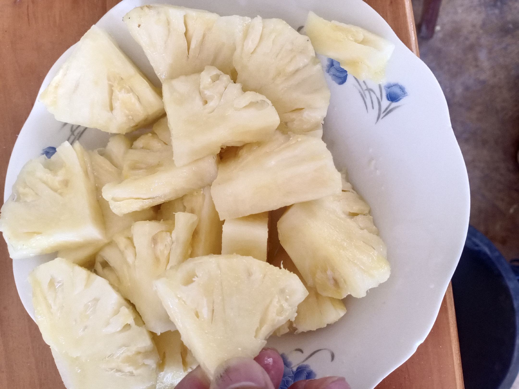 新鲜黄色果肉的菠萝被切成小块,摆放在白色瓷盘中,背景是绿色植物叶片,展示其自然清新的质感,强调食材的新鲜度和可食用性 菠萝切块特写
