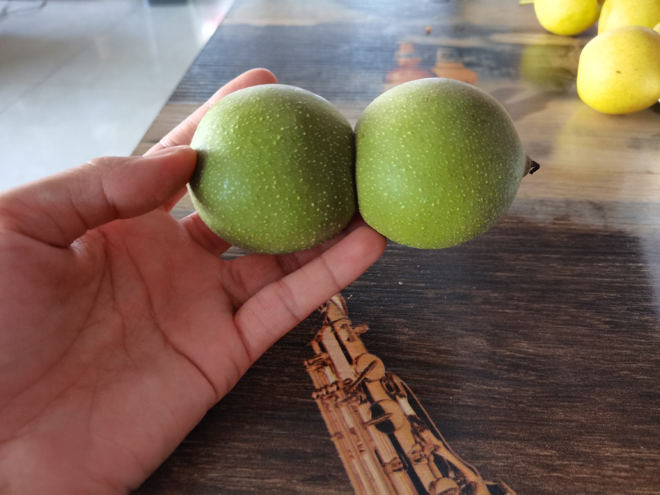 桌面上左侧为带有湿润绿色外皮的新鲜核桃,右侧为已完成去皮的浅棕色硬壳核桃,中间放置一双蓝色橡胶手套和一把不锈钢水果刀,整体布局清晰,突出前后对比效果 一排整齐摆放的新鲜青皮核桃与已去皮的浅棕色硬壳核桃对比图,旁边放置橡胶手套和水果刀