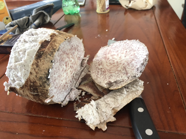 一个完整的荔浦芋头被横向切开,露出内部明显的紫红色槟榔花纹路,肉质洁白细腻,表面湿润有光泽,背景为木质砧板,旁边放置一把不锈钢刀 芋头切开特写