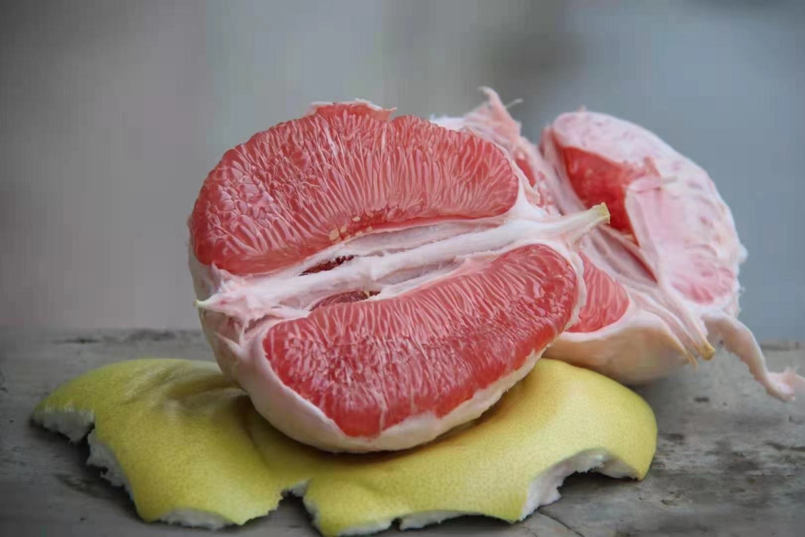 左侧为正宗琯溪蜜柚,果皮黄绿、果形梨状、果肉洁白;右侧为红心柚,果皮偏红、果肉呈粉红至深红色,两者并列对比,旁边放置一张放大镜和一份地理标志认证标签,强调辨识要点 琯溪蜜柚选购对比图