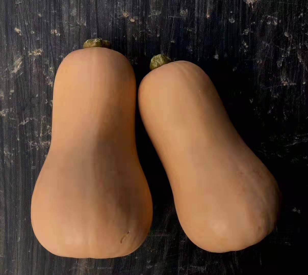 一个完整的奶油南瓜放置在木质厨房台面上,表皮光滑呈浅米黄色,形状为典型的纺锤形,一端带有绿色瓜蒂,背景虚化的环境中有一把不锈钢刀和一块切菜板,光线柔和自然,突出食材的新鲜与质感 奶油南瓜整体外观特写