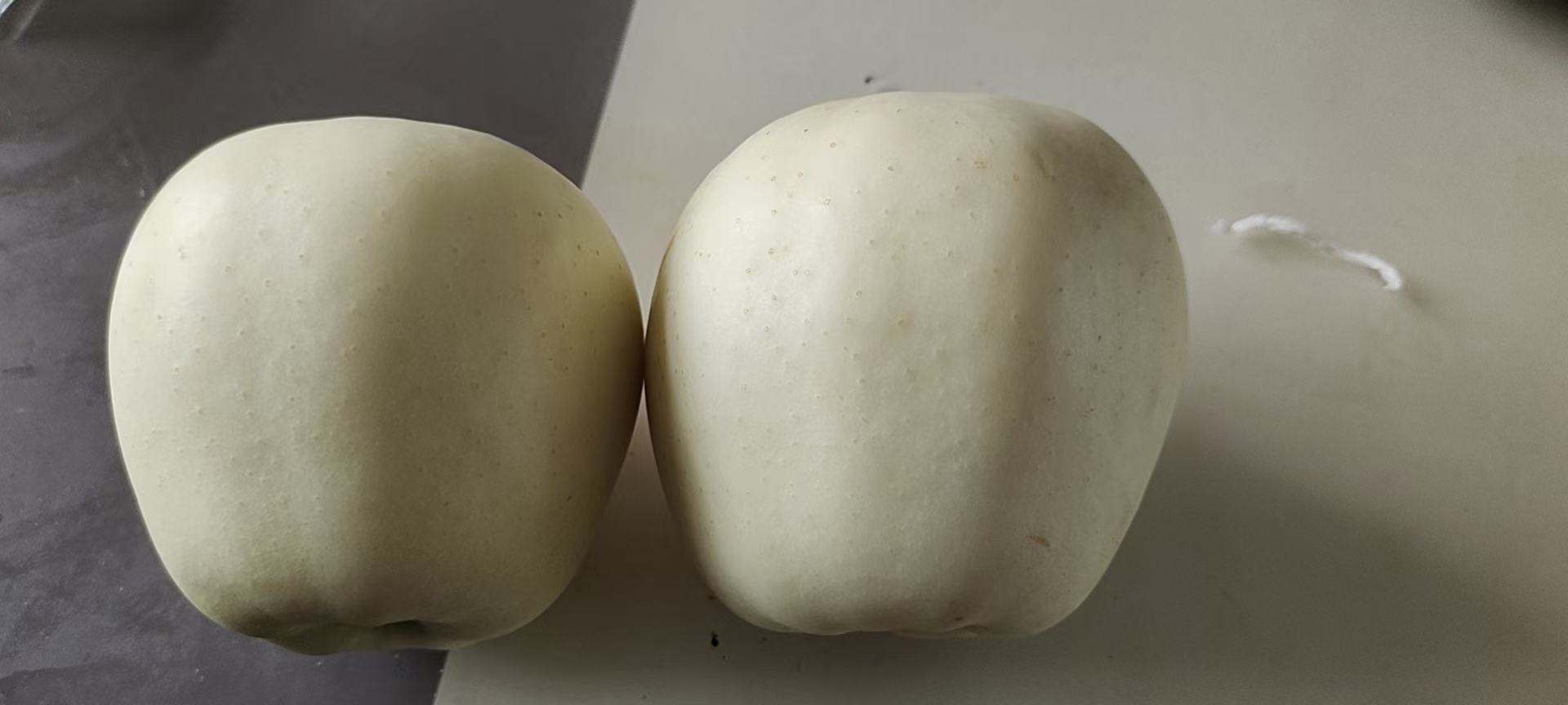 一颗成熟饱满的黄元帅苹果,表皮呈金黄色,带有淡淡红晕,表面光滑有光泽,置于木质砧板上,旁边有一把小刀切开一半,露出洁白细腻的果肉和少量黑色种子,背景为自然光下的果园环境 黄元帅苹果特写