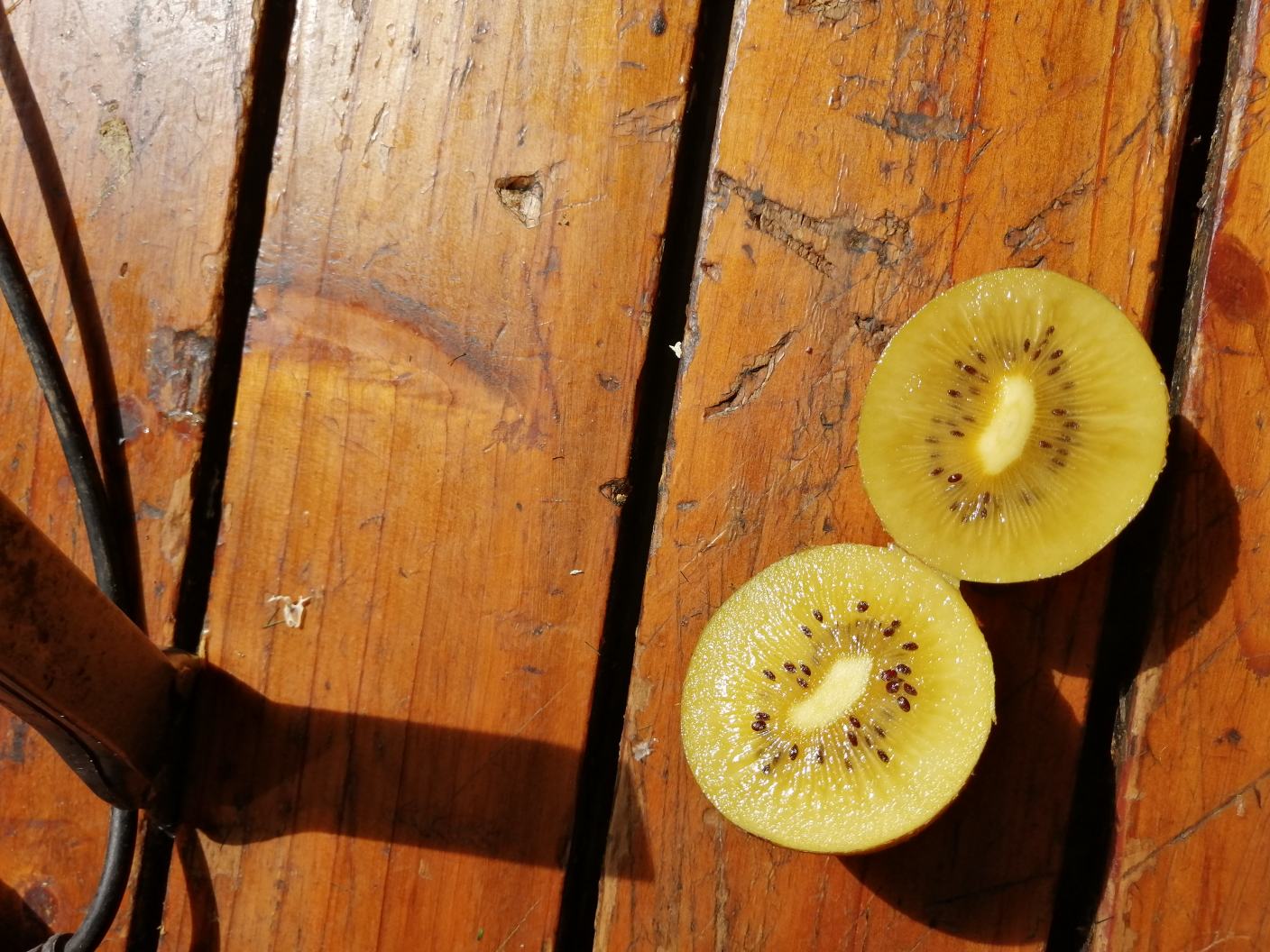 一位孕妇坐在阳光充足的客厅沙发上,手中拿着半个切开的黄心猕猴桃正在食用,旁边小桌上放着一盘新鲜水果拼盘,包含猕猴桃、香蕉和蓝莓,整体氛围温馨健康 孕妇食用黄心猕猴桃场景图