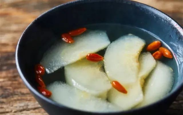 一碗热气腾腾的蒸香梨成品特写,梨肉呈半透明琥珀色,汤汁清澈微黄,枸杞漂浮其中,背景模糊呈现温馨家居氛围 图片描述