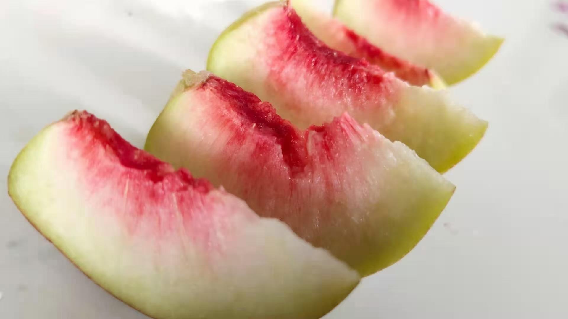 一颗切开的冈山冬桃,果肉呈乳白色,质地紧实,汁水欲滴,果核小且光滑,周围无木质化纤维,果皮薄而完整,边缘有自然裂纹,背景为木质托盘,突显高端水果质感 冈山冬桃果实特写图