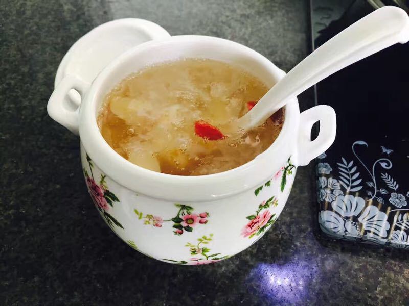 一口白色陶瓷砂锅中正在小火炖煮银耳羹,汤体已呈乳白色微稠状,表面泛着光泽,旁边摆放着冰糖、枸杞和红枣片 炖煮中的银耳羹