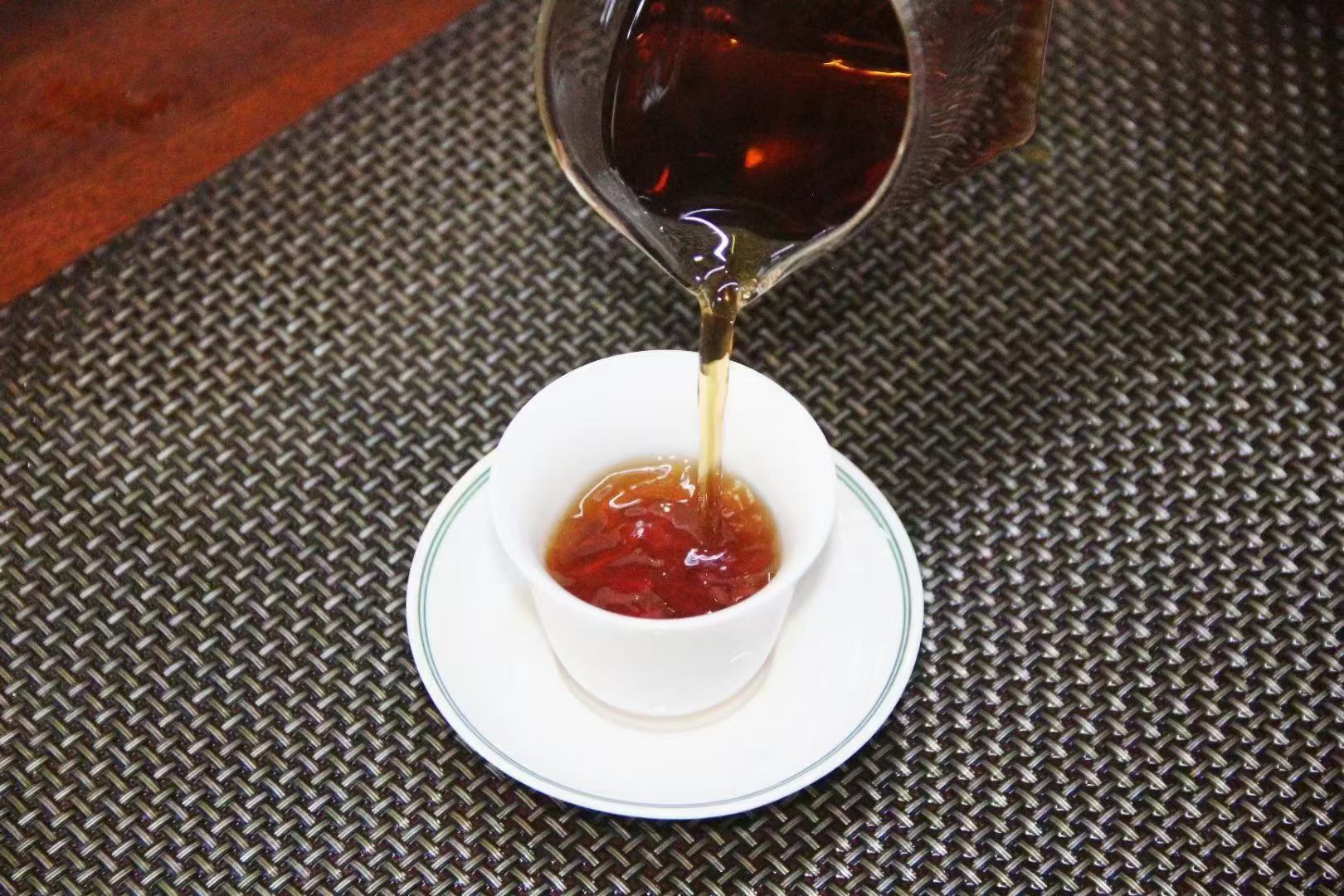 冲泡中的妃子笑茶汤色与叶底：金黄明亮茶汤倾入白瓷盖碗，悬浮细密茶毫；右侧铺开展开的叶底，叶片肥厚柔软、边缘朱红明显，叶脉清晰，呈现典型‘三红七绿’乌龙茶特征