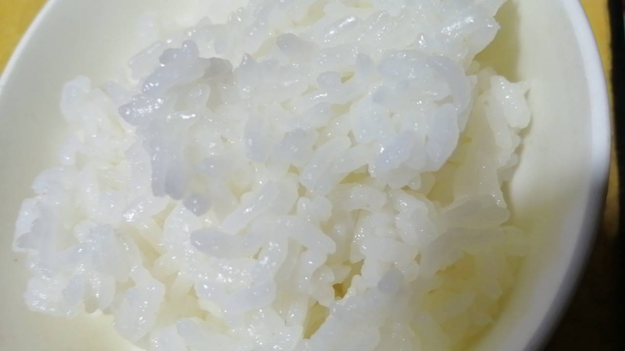 白色陶瓷碗中盛放刚出锅的仙桃长粒香大米,米粒细长晶莹,泛着油润光泽,热气升腾间隐约可见轻盈分离的饭粒结构,背景为稻穗与包装盒组合,突出产品高端形象 仙桃长粒香大米成品展示图