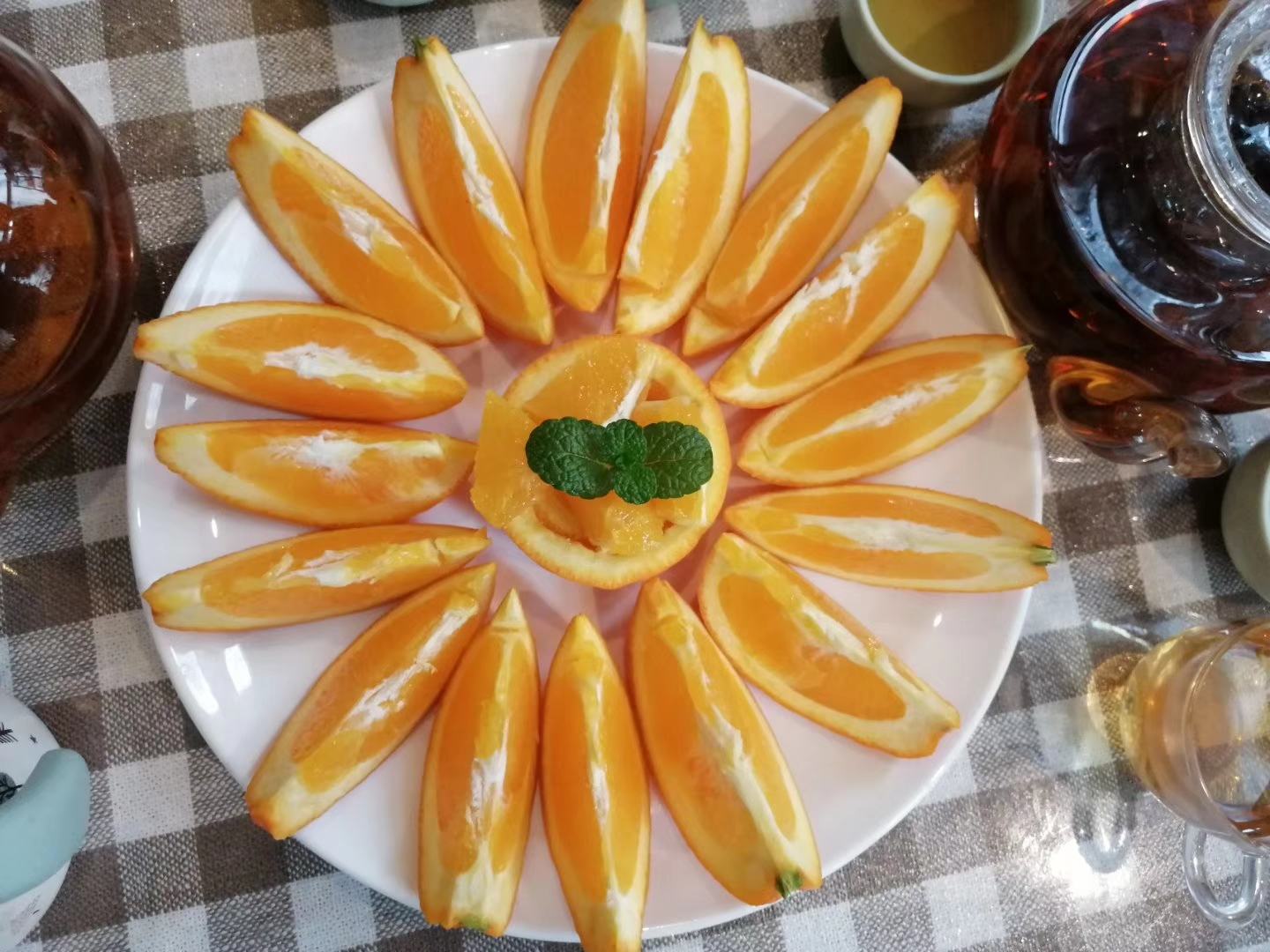 一张木质桌面上摆放着一盒印有‘奉节脐橙’字样的红色精品礼盒,打开后露出六颗完整橙子,旁边是一盘切成薄片的脐橙,果肉晶莹剔透,汁水欲滴,背景虚化的山林景色暗示原产地生态环境 奉节脐橙礼盒与切片对比图