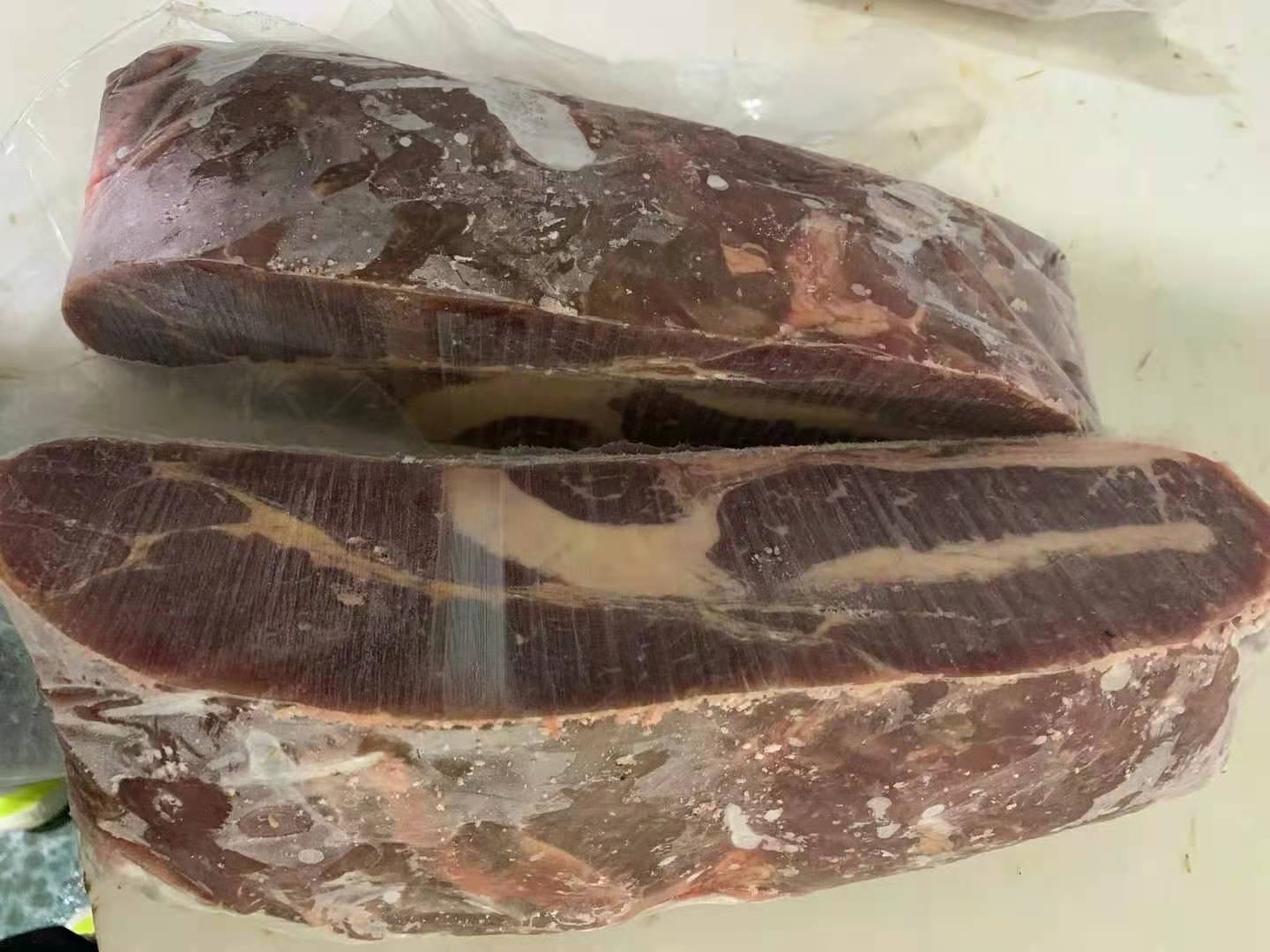 一块新鲜的西门塔尔牛背最长肌被横向切开,露出清晰的大理石花纹,脂肪呈细密网状均匀分布在红色肌肉纤维之间。肉块表面湿润有光泽,边缘带有少量白色脂肪覆盖。旁边放置不锈钢托盘和测量尺,背景为专业肉类加工车间冷柜环境,温度显示为0–4℃ 优质西门塔尔牛肉切割展示图