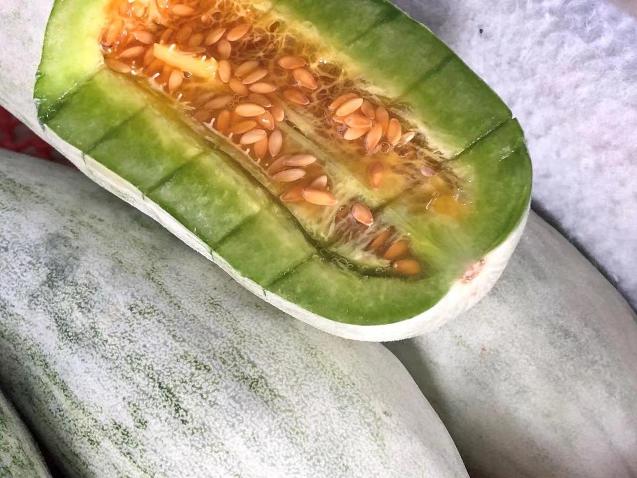 羊角蜜甜瓜横切特写，果肉呈鲜明橘黄色，质地细腻多汁，可见清晰放射状糖纹与少量浅褐色种子，背景为竹编食篮与新鲜薄荷叶