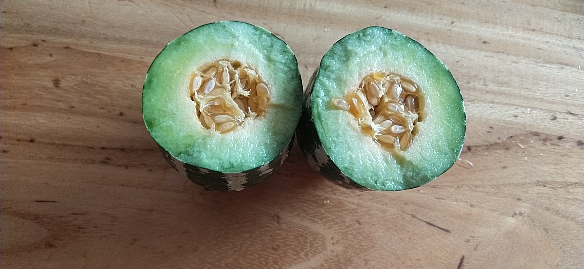 一个完整的博洋9号甜瓜放置在木质桌面上,表面覆盖细腻网纹,切开后露出淡绿色果肉和中心籽腔,果肉饱满多汁,背景为自然光线下的厨房环境 博洋9号甜瓜特写