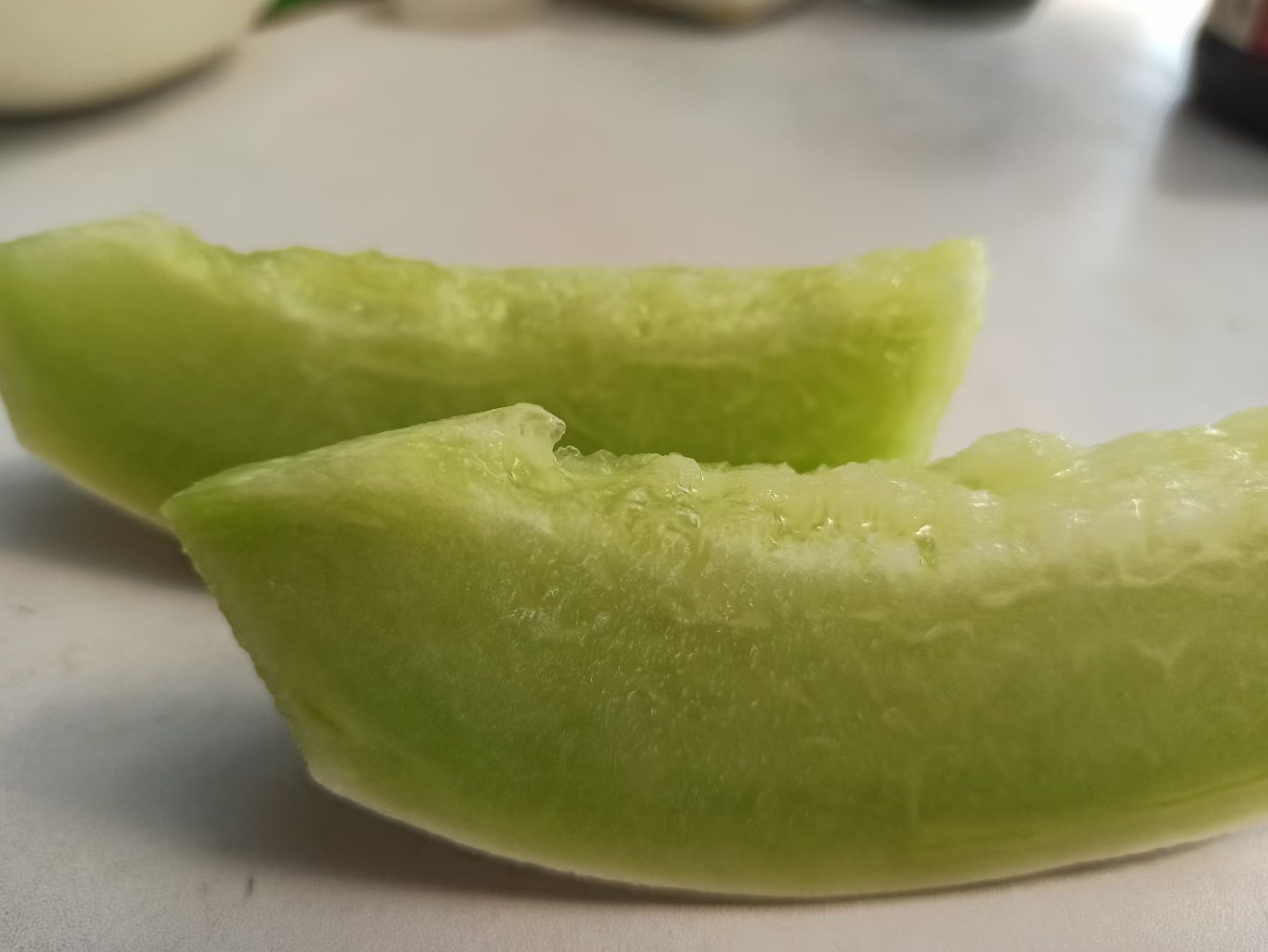 近距离拍摄切开的玉菇甜瓜横截面,展示晶莹剔透的乳白色果肉、清晰的种子腔结构及细腻质地,边缘略有汁液渗出,背景为白色瓷盘,突出食材新鲜感 切开后的玉菇甜瓜横截面近拍