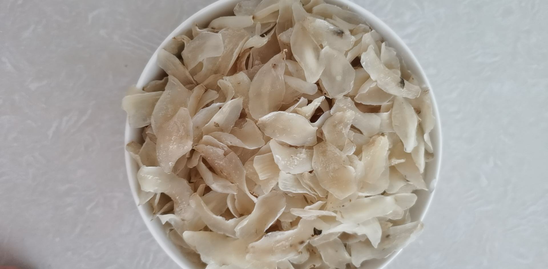 一位主妇在厨房操作台上准备透明玻璃碗,碗中盛有清水和几片切好的百合,旁边放着半个挤过的柠檬,手正将柠檬汁滴入水中,背景可见砧板与百合原材 家庭厨房中正在用柠檬水浸泡切好的百合