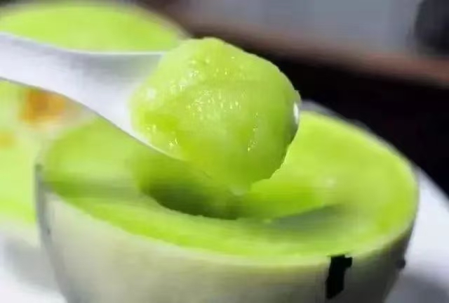 手工制作玉菇甜瓜冰激凌成品图,展现细腻无冰晶的丝绒质地、自然乳白色泽及清新摆盘,突出‘可直接食用’的纯净感 成品玉菇甜瓜冰激凌特写:象牙白柔滑冰糕盛于竹制小碗,表面微泛珠光,插一支薄荷叶,勺尖挖起一小团呈现丝绒拉丝质感