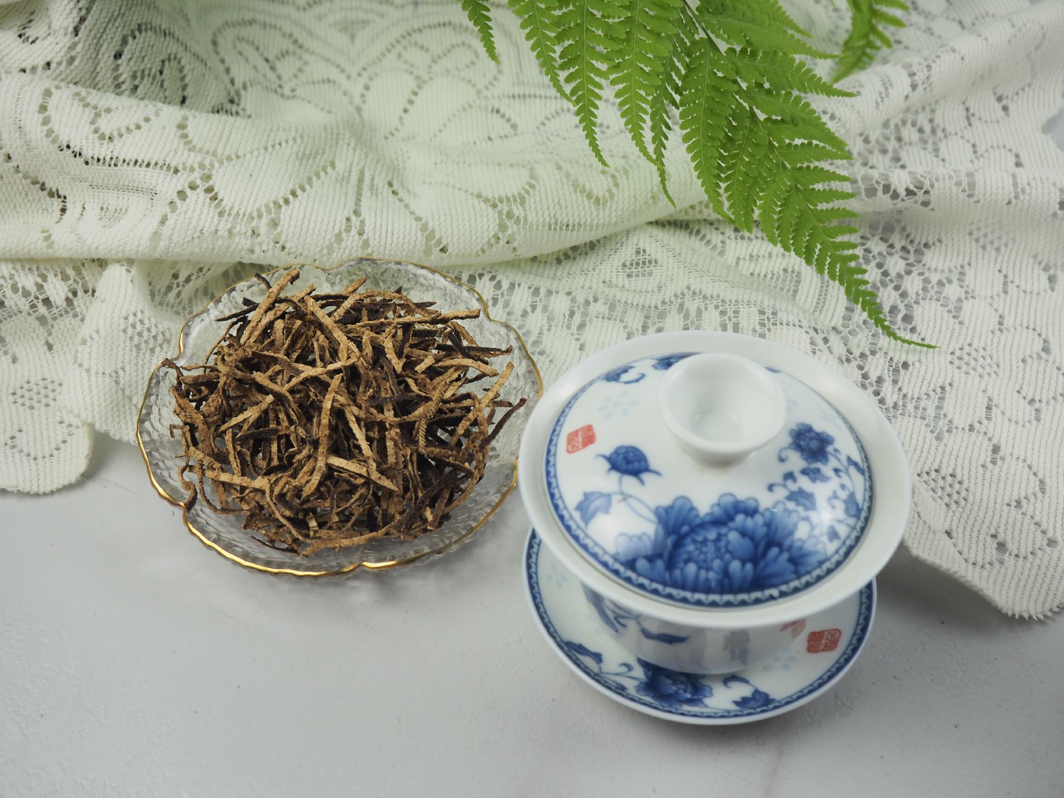 图片说明:玻璃杯中放入切片山楂、陈皮条与苦荞麦粒,倒入热水,茶水呈淡红色,旁边摆放茶具与干料 山楂陈皮苦荞泡水的制作过程