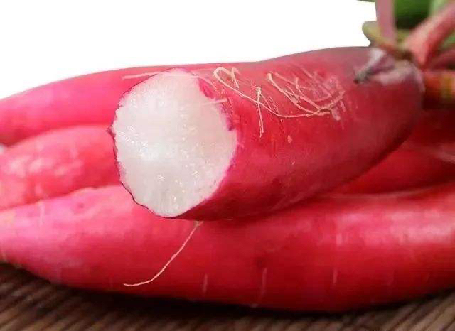 一张高清红皮萝卜的特写图片,展示其鲜红的外皮和洁白的内部结构,背景为自然田园环境 红皮萝卜特写图片
