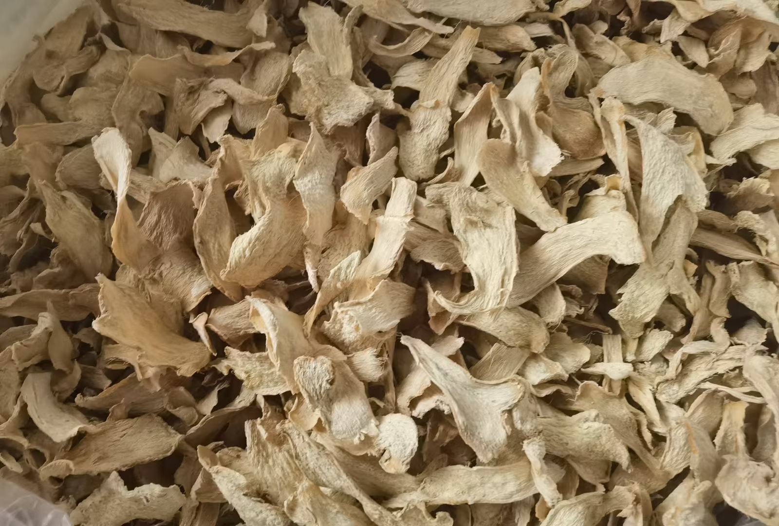 中药师正在标准药斗前称量老姜饮片：不锈钢电子天平显示15.0g，手旁为经净选、切制的标准老姜片（厚2–3mm，边缘微卷，断面色淡黄，无黑心或霉斑），背景可见《中华人民共和国药典》2020年版摊开至“干姜”条目页