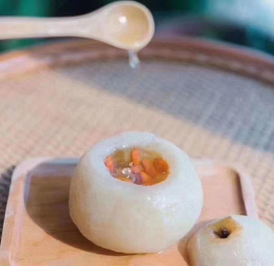 一碗热腾腾的贝母炖雪梨甜品,透明瓷碗中盛放切块的雪梨,中间嵌入一颗完整的浙贝母,汤汁微黄,点缀枸杞,背景为木质餐桌与中式厨房环境 贝母炖雪梨成品图