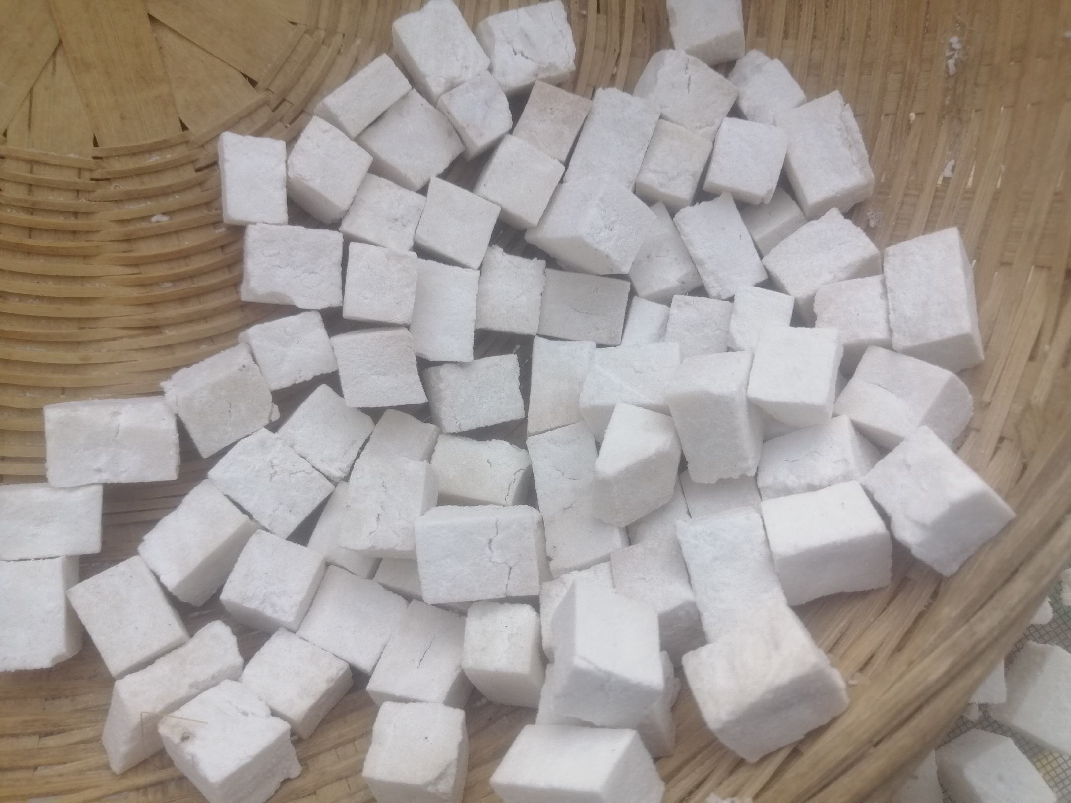 一张俯拍中药台面的照片,中央是一堆去壳的白扁豆,周围环绕着山药片、莲子、薏米、茯苓块等常见健脾药材,所有材料置于圆形竹编托盘上,背景为浅灰色麻布纹理,整体风格自然质朴,突出中医药膳的整体配伍理念 白扁豆与其他中药材组合图