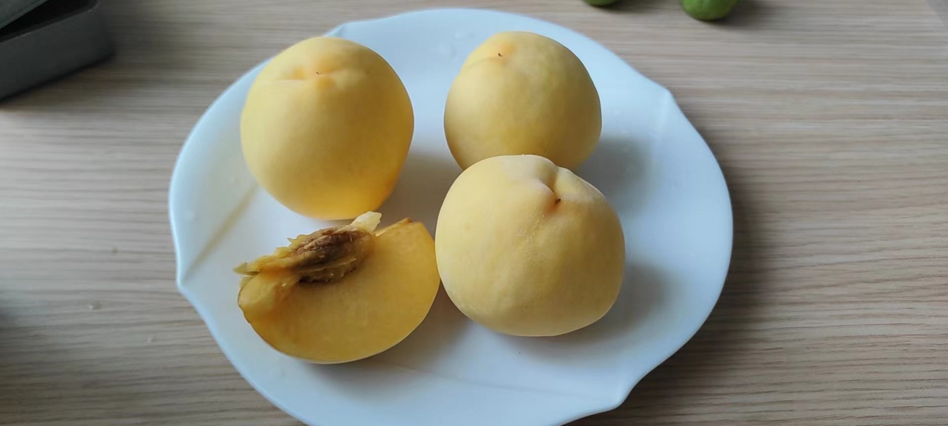 一个被横向切开的新鲜白花桃,露出乳白色的果肉和淡黄色中心,汁液饱满,果核清晰可见,旁边摆放一把不锈钢水果刀和白色瓷盘,背景为木质餐桌 切开的白花桃剖面展示