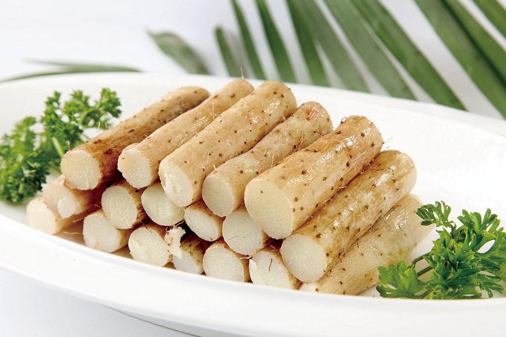 一盘刚出锅的山药炒香芹盛放在白色圆形瓷盘中央,山药片与香芹段交错分布,表面泛着自然油光,旁边点缀两片柠檬片和少许红椒丝作为装饰,背景为简约中式餐桌 成品装盘俯拍图