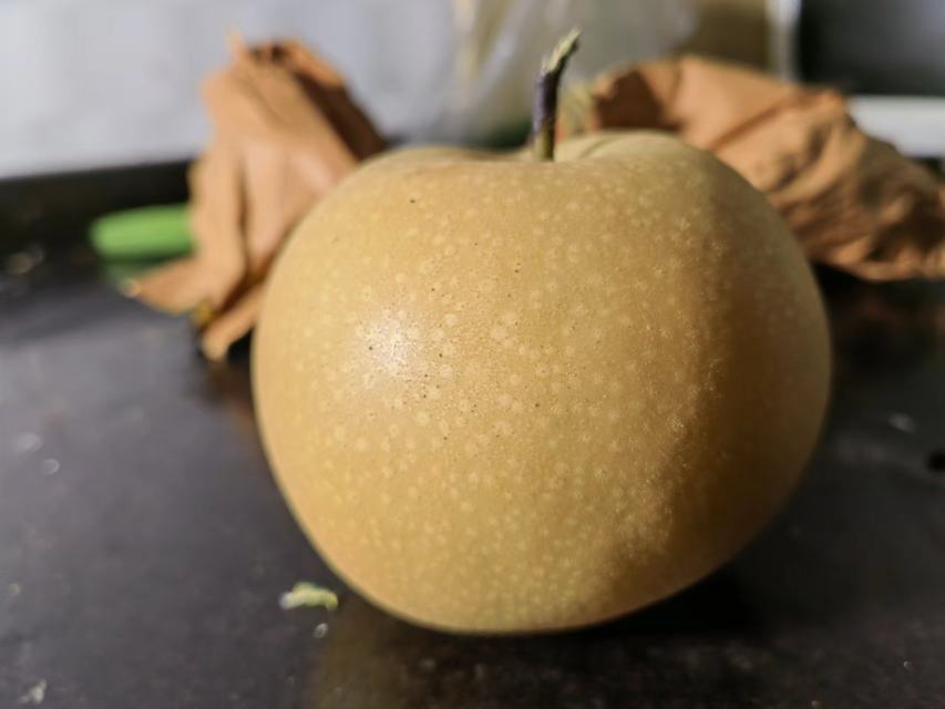 一个完整的秋月梨放置在浅色竹编果篮中,果皮呈黄褐色带麻点,表面光洁有蜡感,果柄绿色新鲜,镜头聚焦于果实底部,清晰展现平坦的花萼疤痕和放射状细密纹路,背景虚化体现自然田园氛围 单个优质秋月梨特写