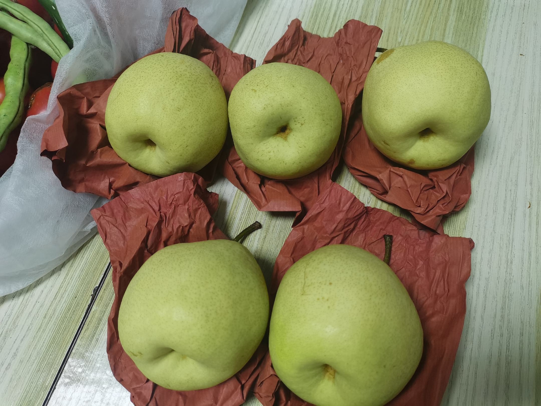 一张木质桌面上陈列着多种酥梨衍生产品:玻璃瓶装的透明梨汁、陶瓷罐中的黑色梨膏、真空包装的冻干酥梨片、礼盒装的精品鲜梨,旁边配有绿叶装饰和手写标签,整体呈现自然健康的产品风格 酥梨系列产品展示