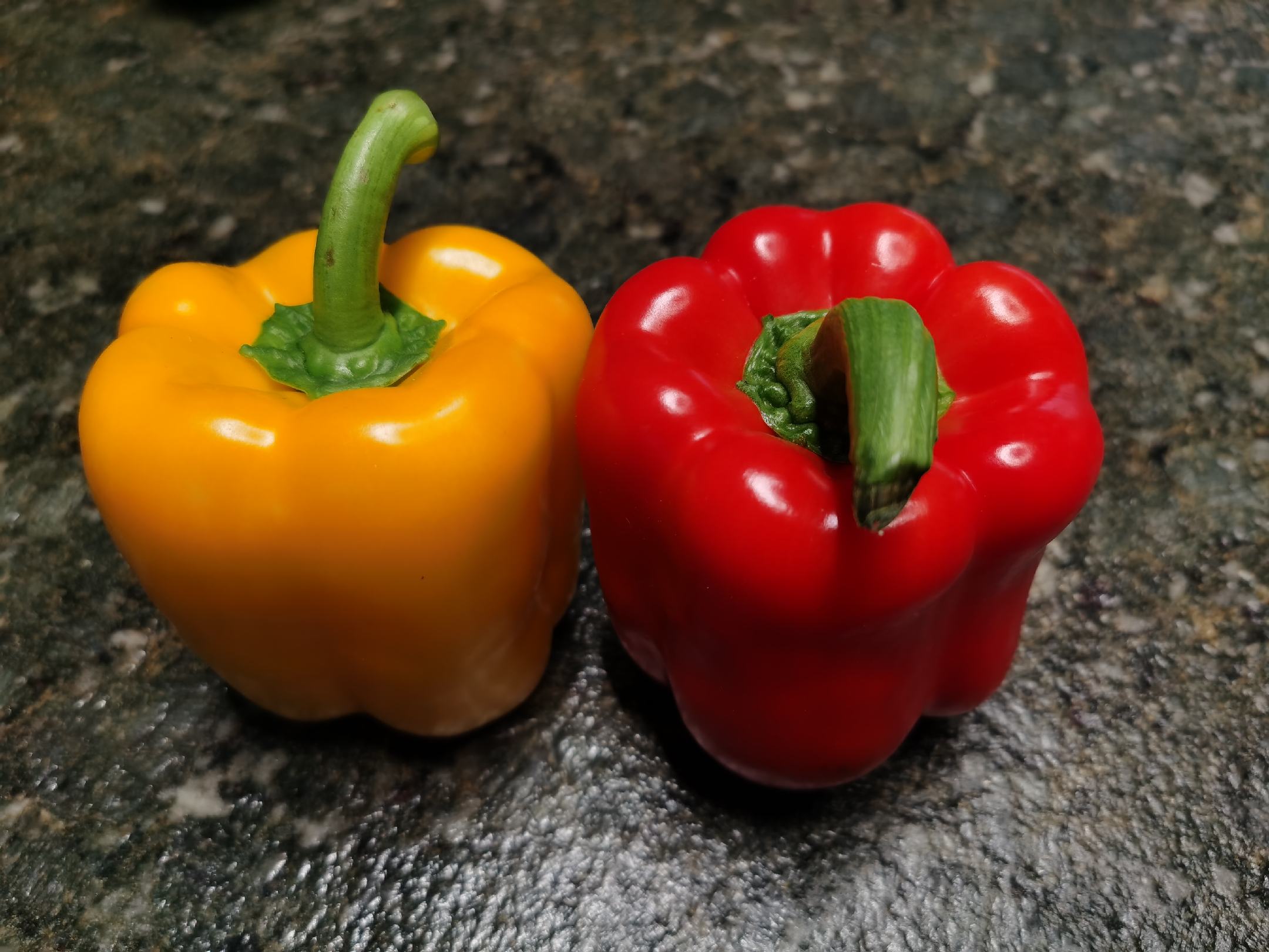 厨房实操对比图：左半边为切配好的青绿色方形甜椒丁（颗粒均匀、色泽鲜亮、边缘无汁液渗出）；右半边为斜切成段的青绿色尖椒（段长约2cm、断面可见白色胎座与少量种子、边缘微透明）；两者分置白瓷盘，背景为不锈钢灶台与中式炒锅