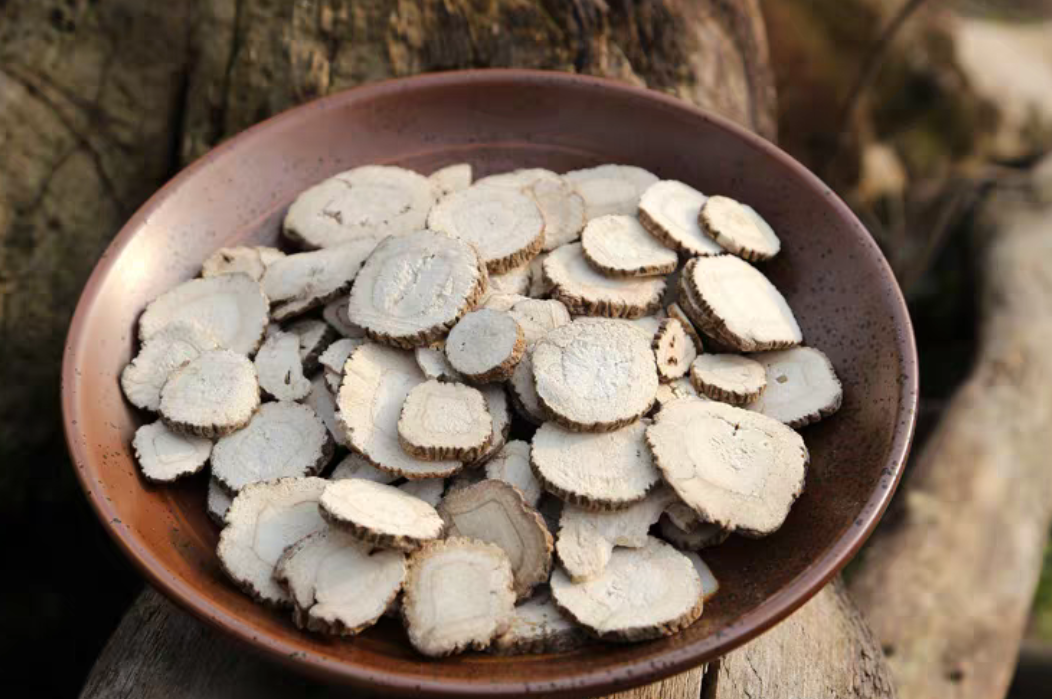 中医师在药斗前取用白芷饮片：木质中药柜上标有“白芷”铜牌，药师手持小铜勺从抽屉中取出淡黄棕色切片状药材，背景可见《中国药典》与传统中药处方笺