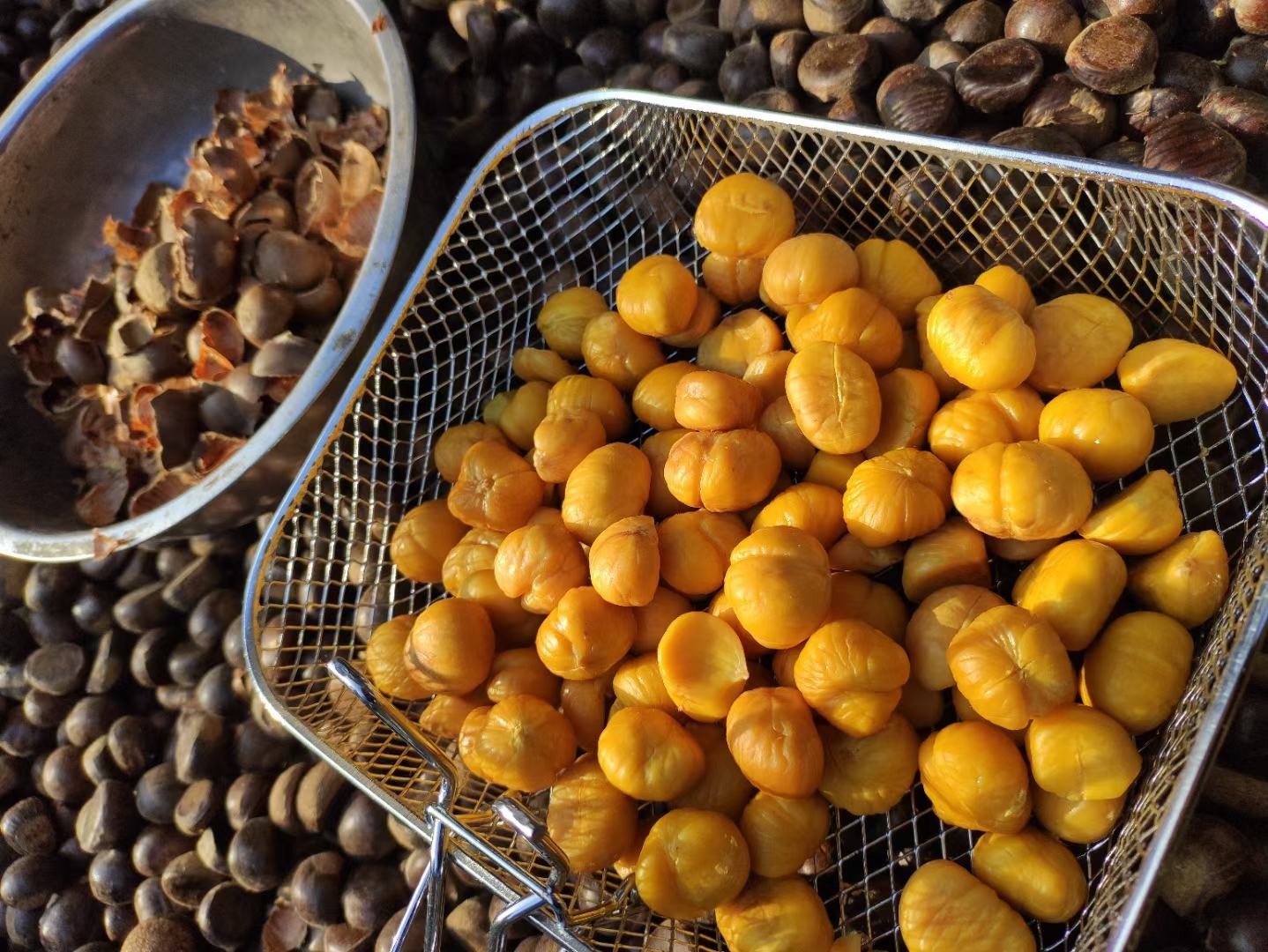 一位家庭主妇正在厨房操作台上将蒸熟的迁西板栗去壳碾压成细腻的黄色泥状物,旁边放置搅拌碗、勺子和新鲜板栗壳,展现家庭健康料理场景 家庭厨房中用迁西板栗制作板栗泥的过程