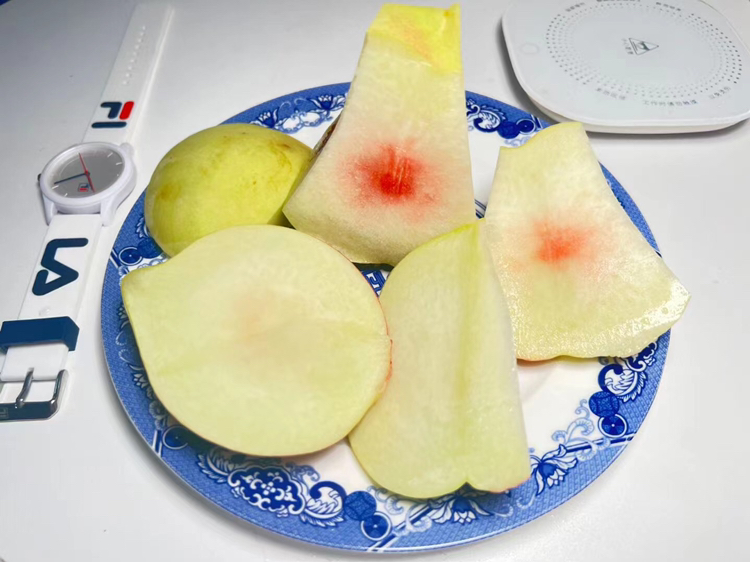 一颗成熟饱满的中华寿桃,表皮呈粉红色带绒毛,果体圆润硕大,切开后果肉呈淡黄色,汁水丰富,旁边摆放一把不锈钢水果刀和砧板,背景为木质料理台面 中华寿桃特写
