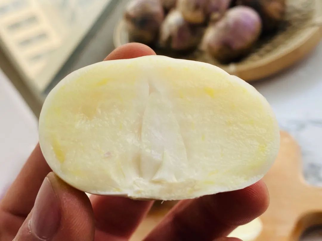 一颗完整的独头蒜,外皮呈浅褐色,表面光滑,剥开后露出洁白饱满的单一蒜瓣,背景为木质餐桌,旁边摆放着几片切开的蒜肉,展示其内部结构 独头蒜实物特写