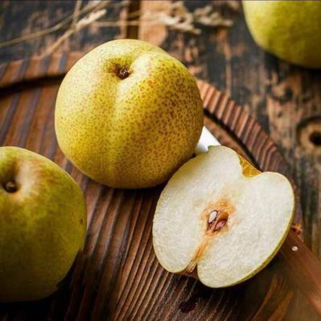 一颗完整的冻酸梨放置在木质托盘上,表皮呈深褐色至近黑色,表面覆盖一层薄薄的冰霜,光线反射出晶莹质感;旁边配有半剖开的冻梨,可见内部果肉为浅棕色、质地绵软湿润,汁水丰富 冻酸梨成品特写